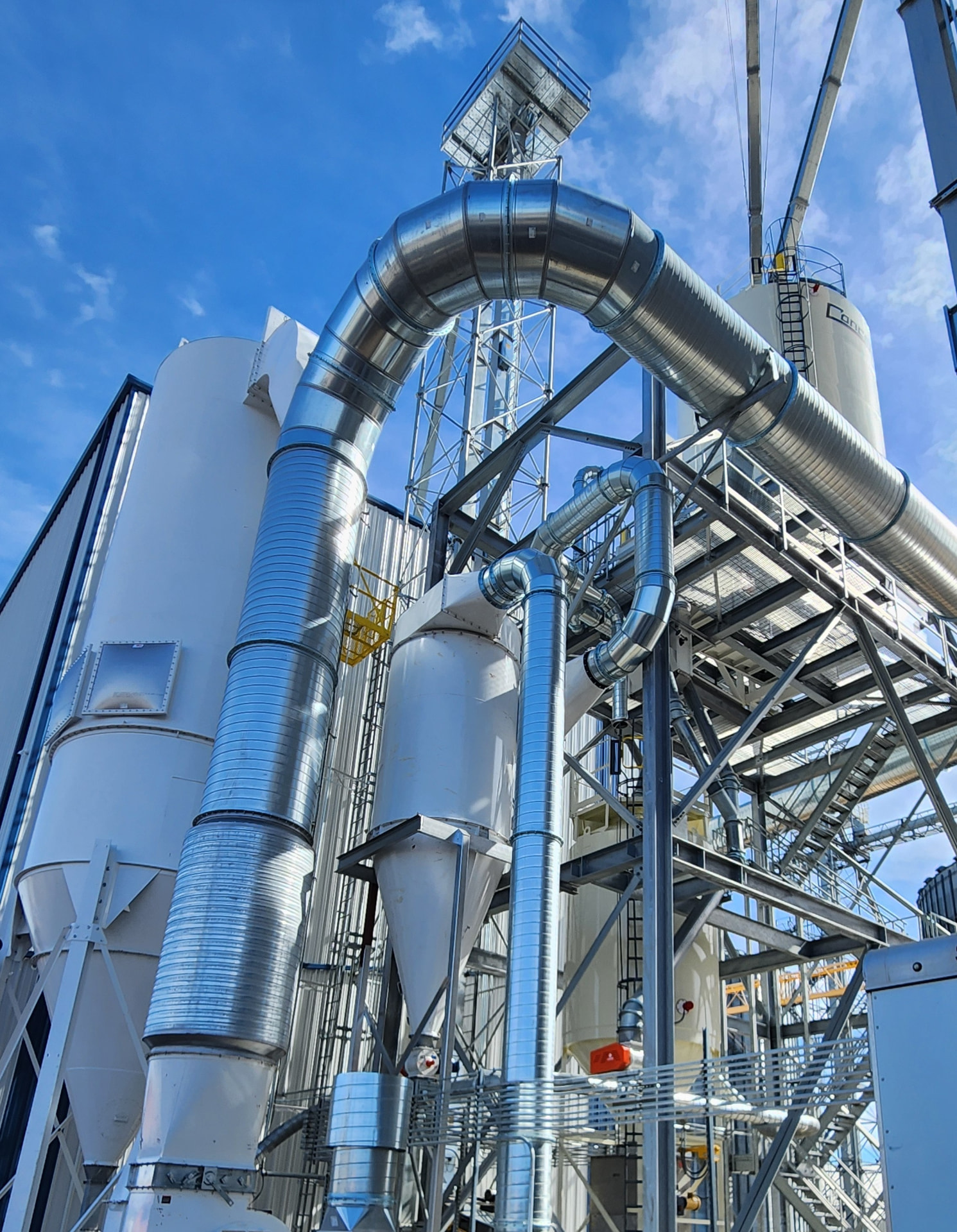 Grain-processing facility ductwork, cyclones, and storage vessels rising against a blue sky