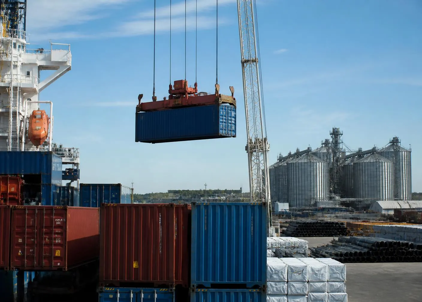 Shipping containers being loaded at a port terminal beside grain storage silos